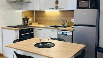 Een moderne keuken met witte kasten, een houten eettafel, zwarte stoelen, een ingebouwde oven, een vaatwasser en een magnetron.