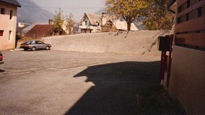 A parking lot with a car, a building with a sloped roof, and a tree with yellow leaves.