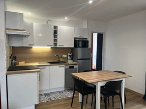 A compact kitchen with white cabinets, a wooden countertop, a sink, a stove, and a refrigerator. There is a dining table with chairs.