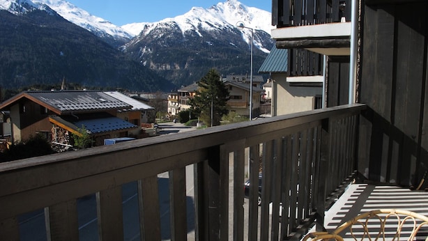 Ein Balkon mit Blick auf schneebedeckte Berge, ein Korbstuhl und ein Gebäude mit schrägem Dach.