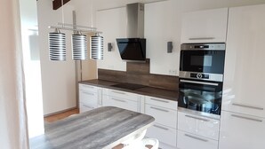 Une cuisine moderne avec des meubles blancs, un four encastré, un four à micro-ondes et un plan de travail en bois.
