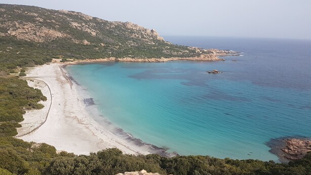 Un paysage côtier caractérisé par une plage de sable, des eaux turquoise et limpides, et des falaises rocheuses.