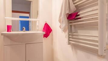Un baño con lavamanos blanco, espejo y toallero.