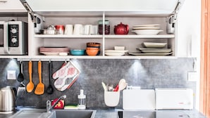 A kitchen with a built-in oven, a coffee machine, and a sink. There are shelves with dishes and utensils.