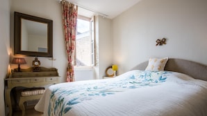 A bedroom with a bed, a dresser, a mirror, a window with curtains, and a wall clock.
