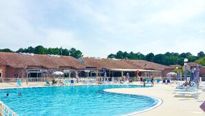 A swimming pool with lounge chairs and umbrellas, surrounded by buildings with a tiled roof. - PROMO ☀️☀️☀️ LES VILLAS DU LAC, swimming pool, tennis, petanque, mini golf (Soustons)