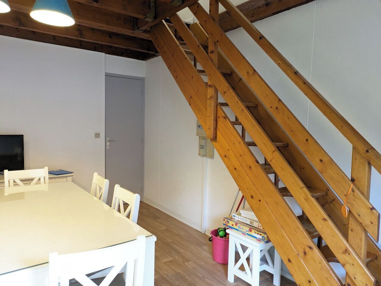 A room with a wooden staircase, a white table with chairs, and a door.
