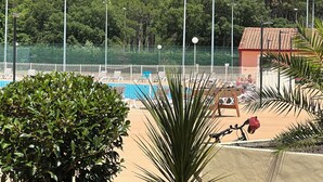 A pool area with lounge chairs and a fenced tennis court. - PROMO ☀️☀️☀️ LES VILLAS DU LAC, swimming pool, tennis, petanque, mini golf (Soustons)