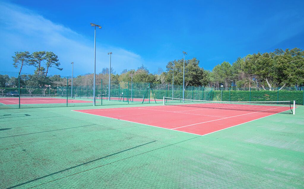 A tennis court with green and red surfaces, surrounded by trees and fencing.