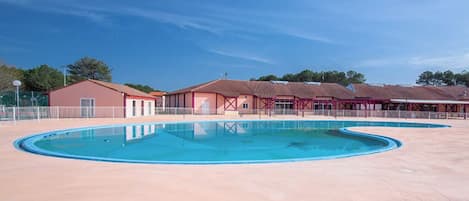 A swimming pool with a curved design, surrounded by buildings with red roofs and a clear blue sky.