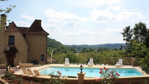 Zona de piscina con sillones de descanso, un edificio de piedra y vistas a un lago y montañas.