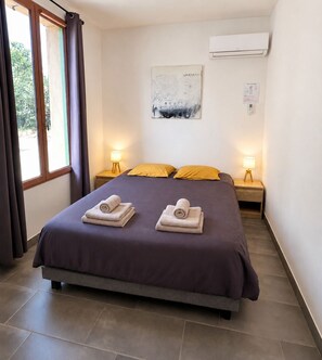 Une chambre d’hôtel avec un lit, deux lampes de chevet, un climatiseur, un tableau au mur et une fenêtre avec des rideaux.