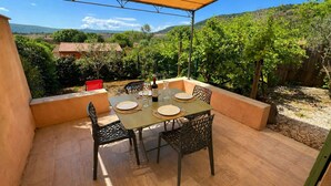 An outdoor patio with a table set for dining, surrounded by chairs, and a view of the countryside.