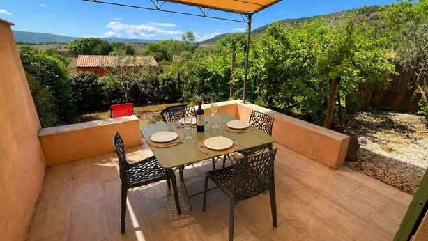 An outdoor patio with a table set for dining, surrounded by chairs, and a view of the countryside. - Quiet Salagou cottage with lovely view over the valley (Octon)