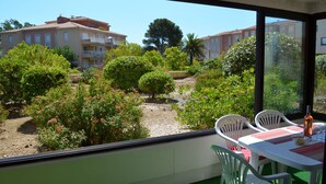 A balcony with a table and chairs, overlooking a garden with various plants and a building in the background. - Quiet air-conditioned apartment 10 minutes' walk from the beaches and shops (Bormes-Les-Mimosas)