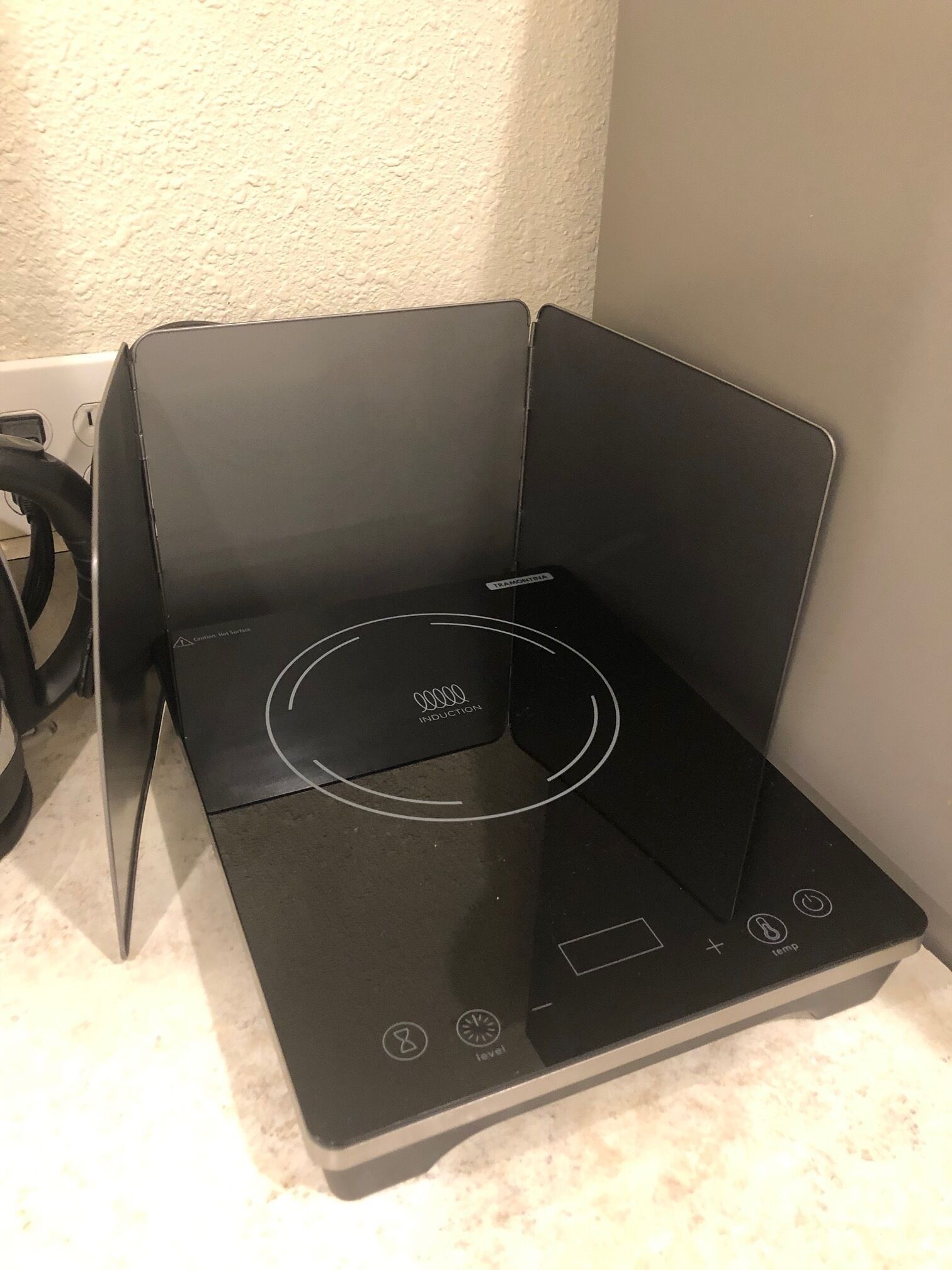 Une plaque de cuisson à induction noire, dotée d’un panneau de commande, d’un câble d’alimentation et d’une prise murale.