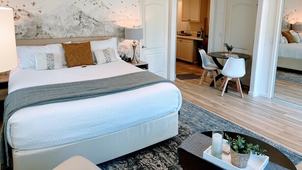 Une chambre d’hôtel moderne avec un grand lit, un ventilateur de plafond, un coin repas et une cuisine en arrière-plan.