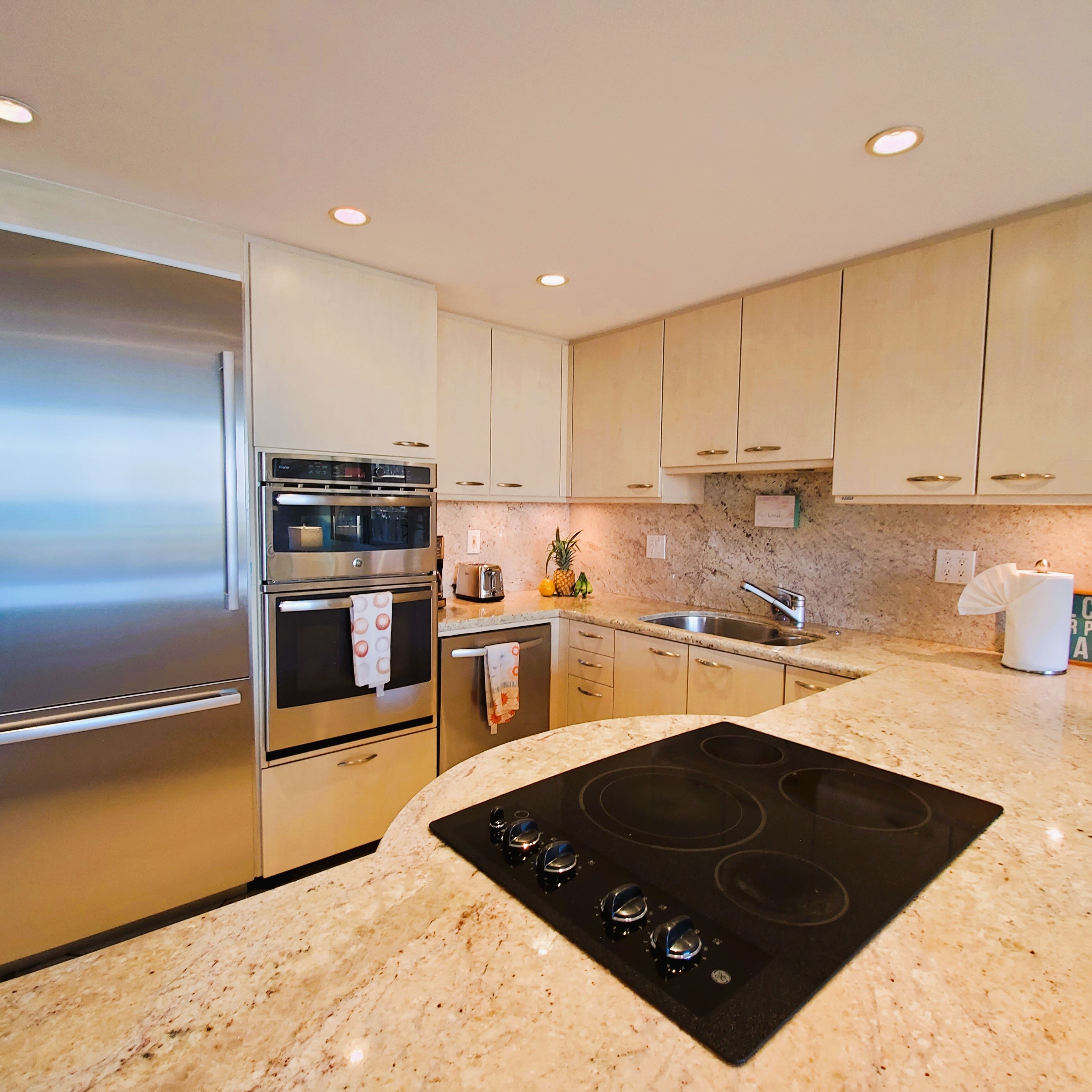 A modern kitchen with stainless steel appliances, granite countertops, and beige cabinetry.