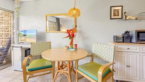 A dining area with a round table, two chairs, a vase of flowers, a television, a microwave, and a cabinet.