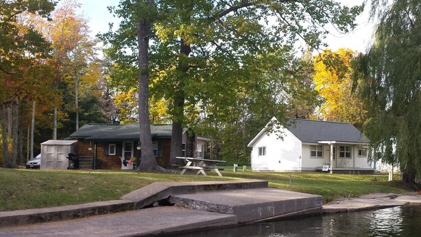 Una cabaña junto al lago con un muelle, una mesa de picnic y un cobertizo pequeño.