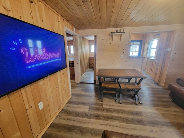 A wooden interior with a neon 'Welcome!' sign, a wooden table, and a bench.