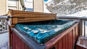 Een hottub met een houten buitenkant en een blauw, marmerachtig interieur, omringd door sneeuw.