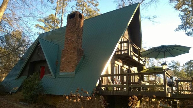 A cabin with a sloped roof, a brick chimney, and a deck with outdoor seating.