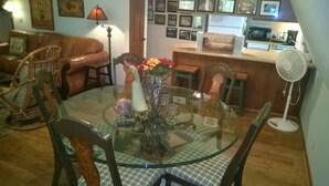 A dining area with a glass table surrounded by chairs, a vase with flowers, and a lamp.