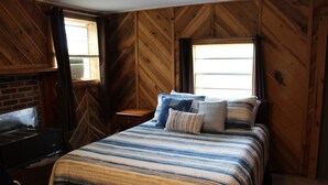 Una habitación con una cama, pared de madera, ventana y chimenea.