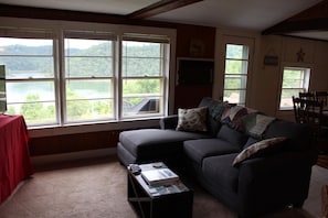 A living room with a couch, a coffee table, and a view of a lake through large windows.