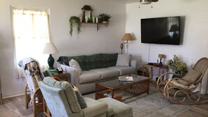 A living room with a sofa, armchairs, a coffee table, a television, and a ceiling fan. - Cosy Home with Heated Pool (Edgewater)