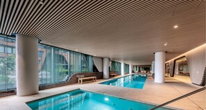 Una piscina interior moderna con techo inclinado, ventanas amplias y un banco a lo largo de la piscina.