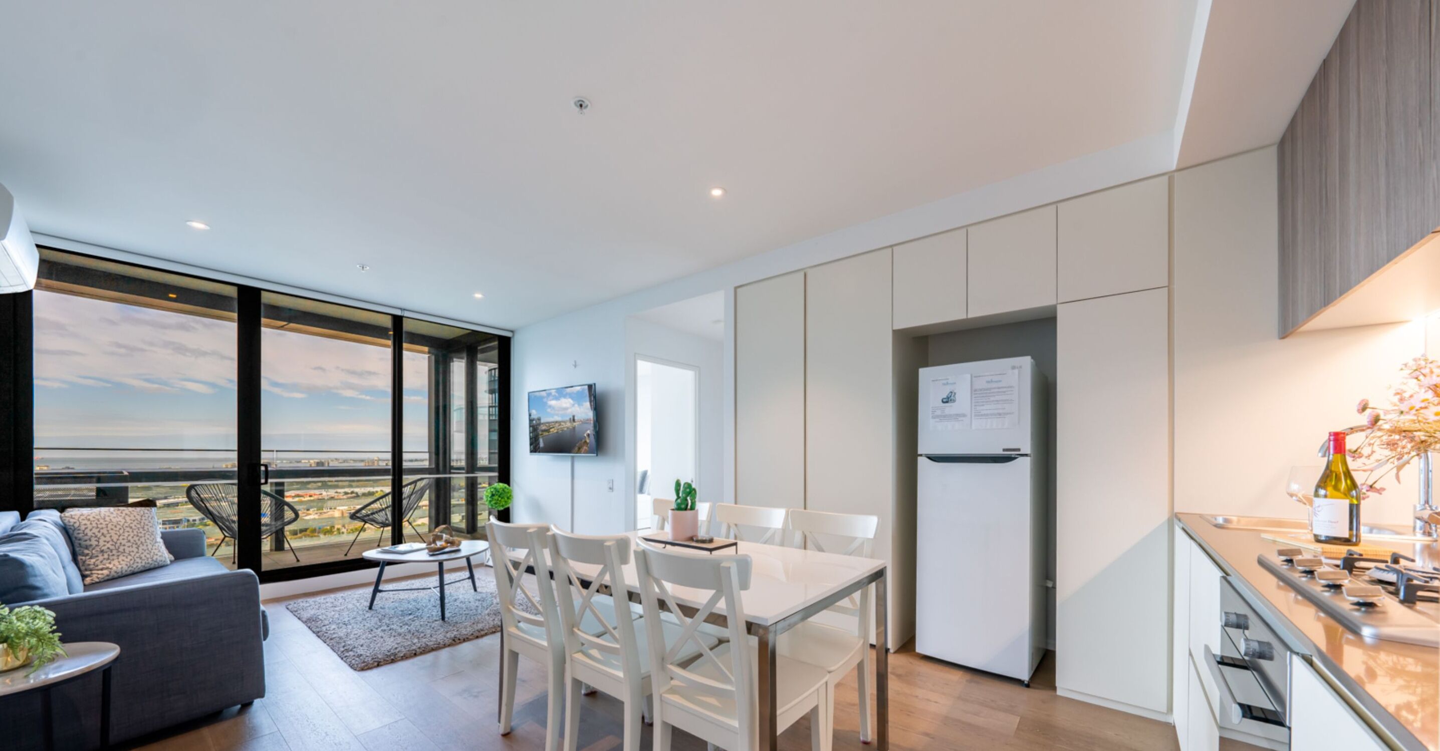 A modern apartment with a dining area, kitchen, and a large balcony with a city view.