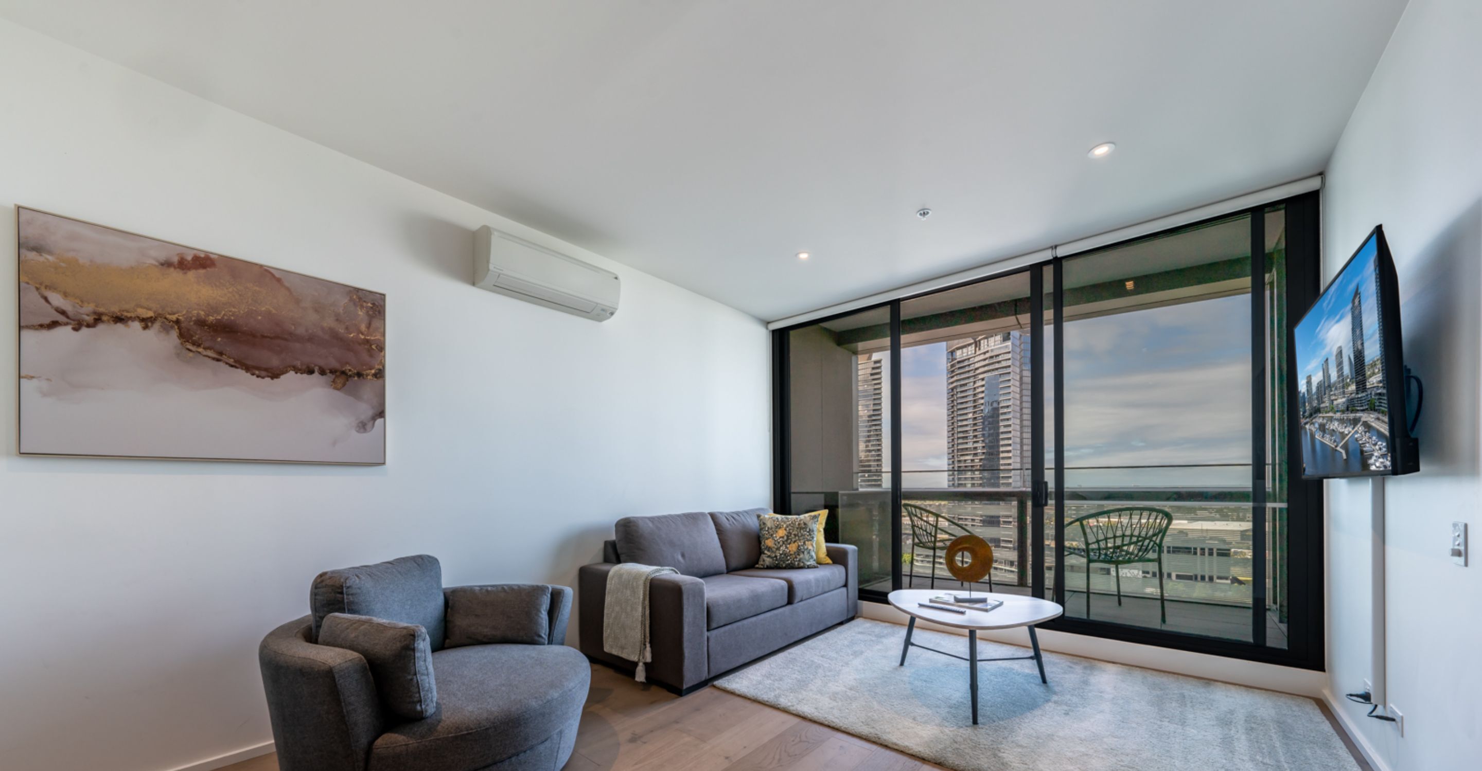 A modern living room with a gray sofa, a gray armchair, a round coffee table, and a large window offering a city view.