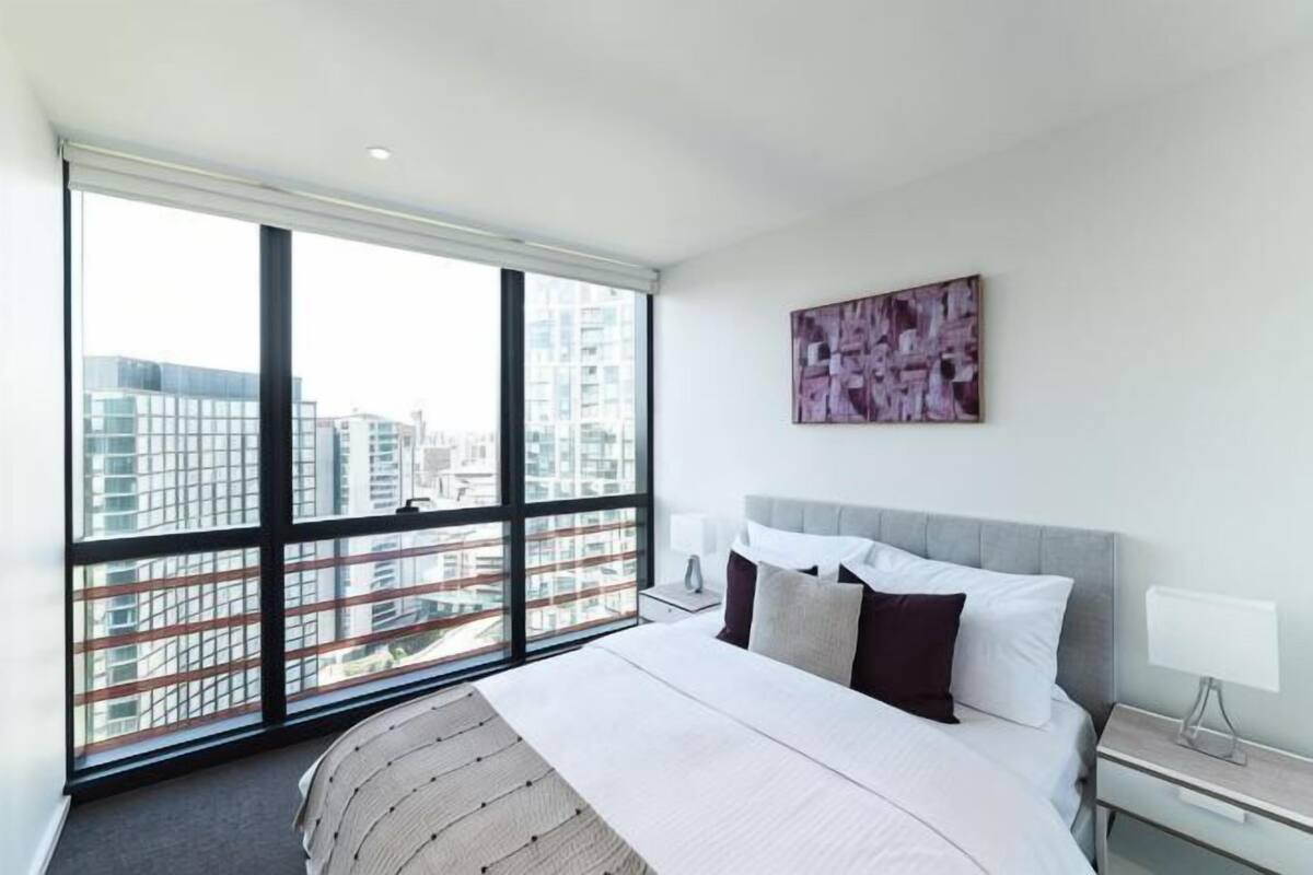 Ein modernes Hotelzimmer mit einem großen Fenster, einem Bett mit weißer Bettwäsche, einem grauen Kopfteil und einem Wandbild.