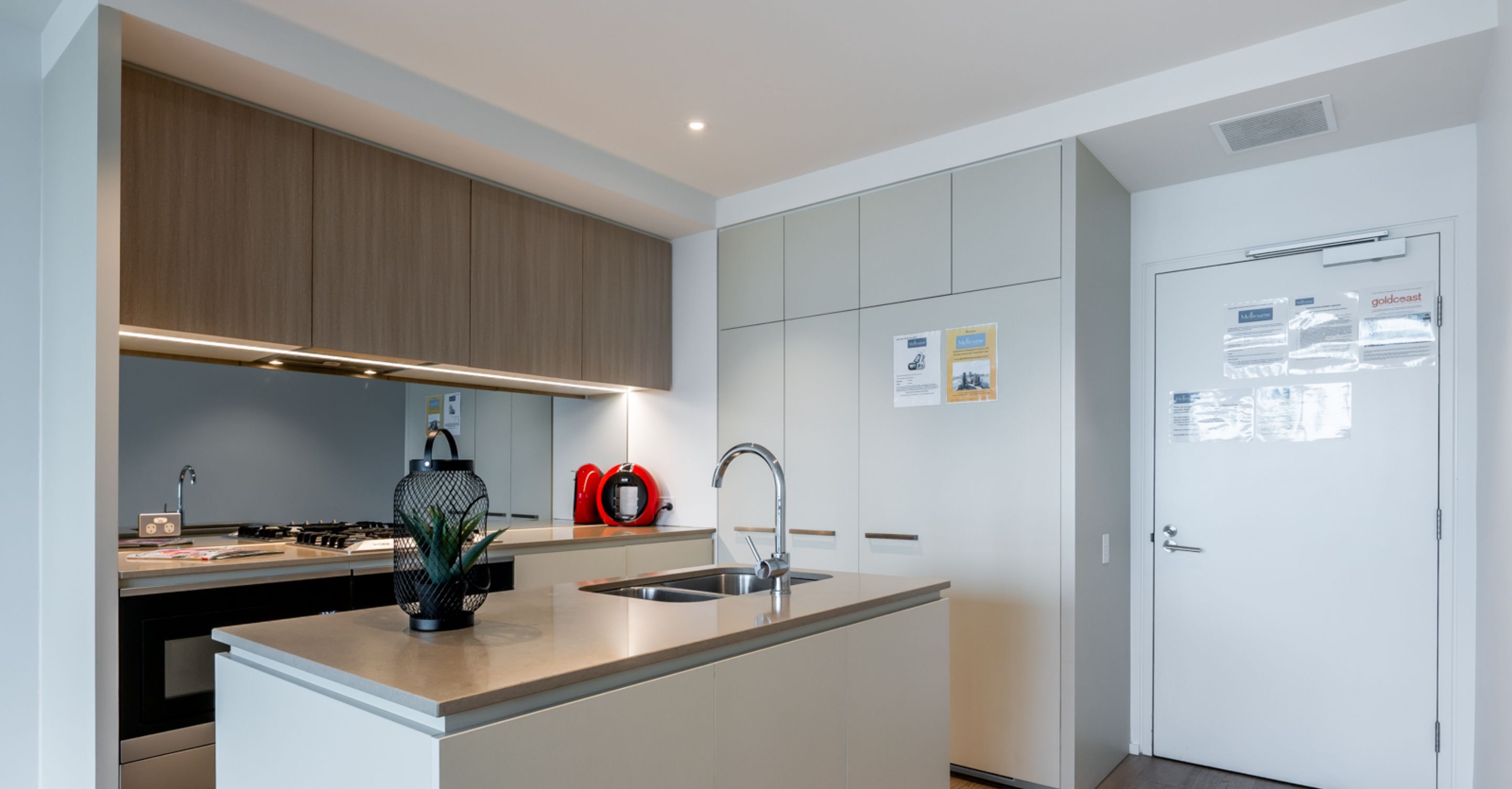 Une cuisine moderne dotée d’un îlot central, d’appareils électroménagers en acier inoxydable et d’une porte blanche agrémentée d’un panneau d’affichage.