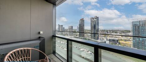 A balcony with a view of a cityscape, a wicker chair, and a glass railing.