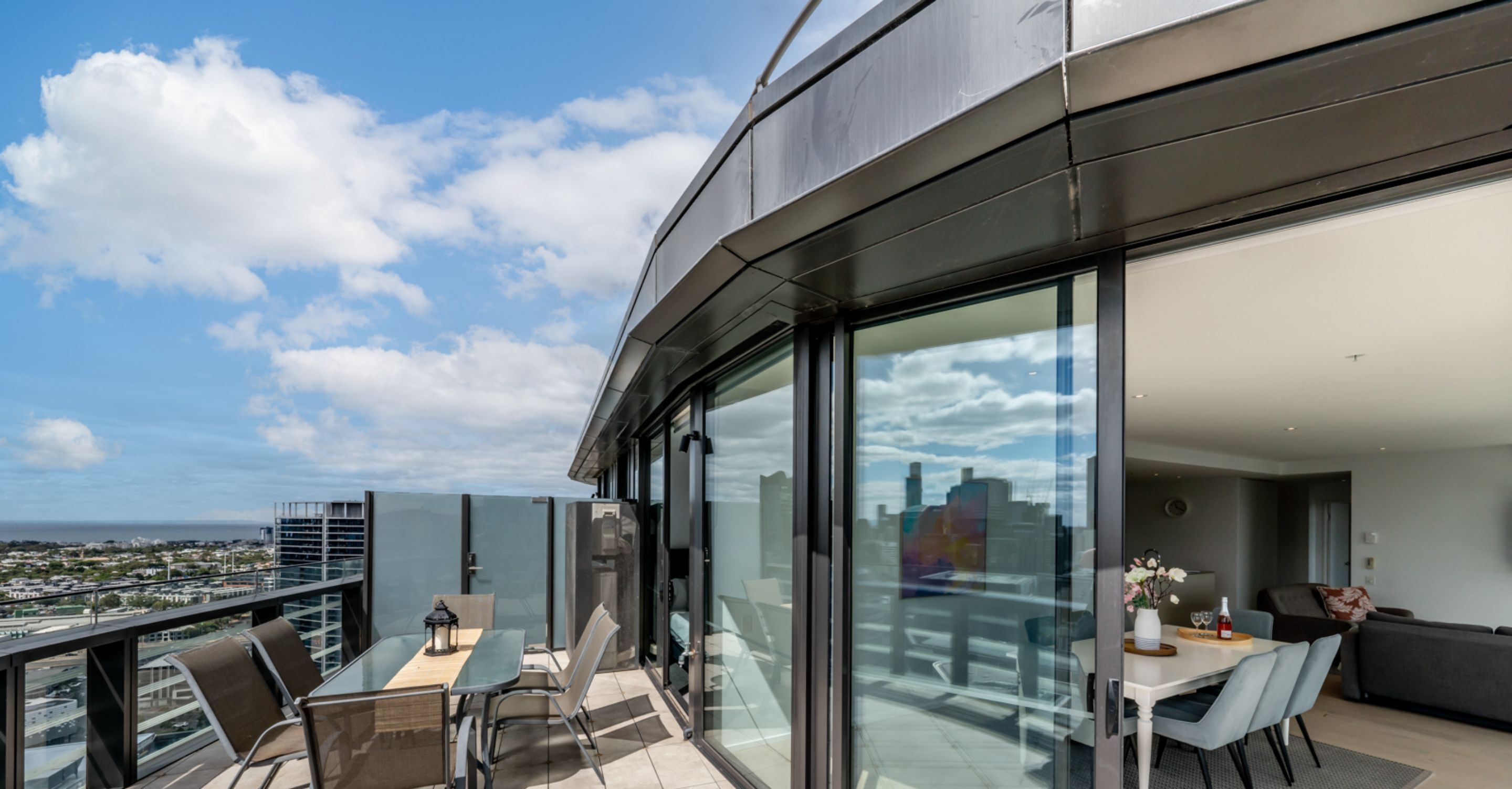 Ein moderner Balkon mit Glasgeländer, einem Esstisch und Stühlen.