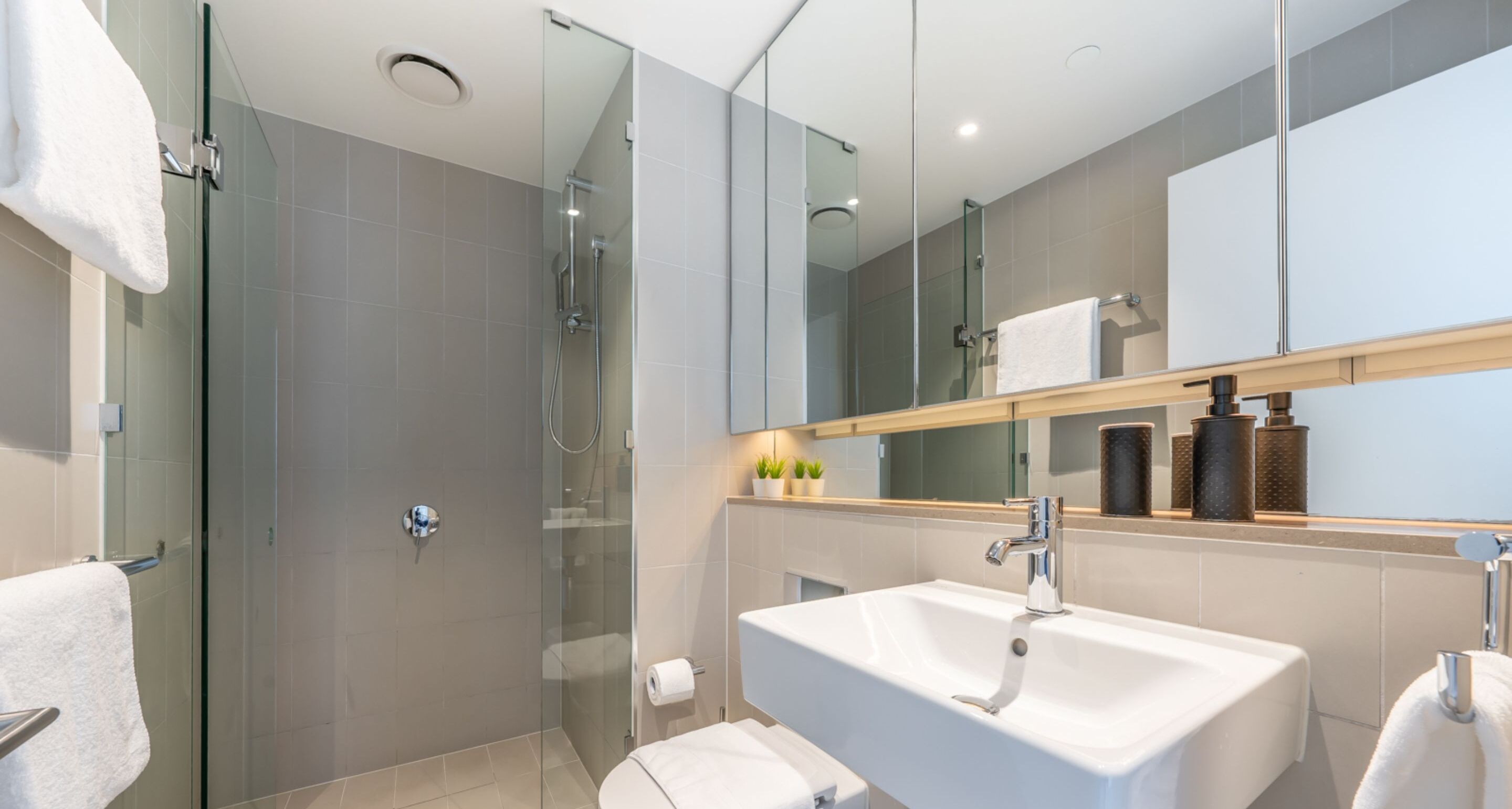 A modern bathroom with a glass-enclosed shower, a white sink, and a large mirror.