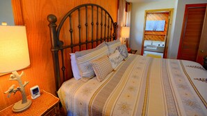 Un lit bien fait, avec une couvre-lit à motifs, une tête de lit en bois et une table de chevet sur laquelle se trouvent une lampe et un petit objet décoratif.