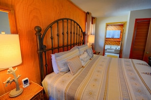 A neatly made bed with a patterned bedspread, a wooden headboard, and a bedside table with a lamp and a small decorative item.