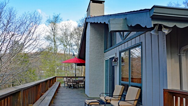 Une terrasse en bois avec des sièges d’extérieur et un parasol rouge.