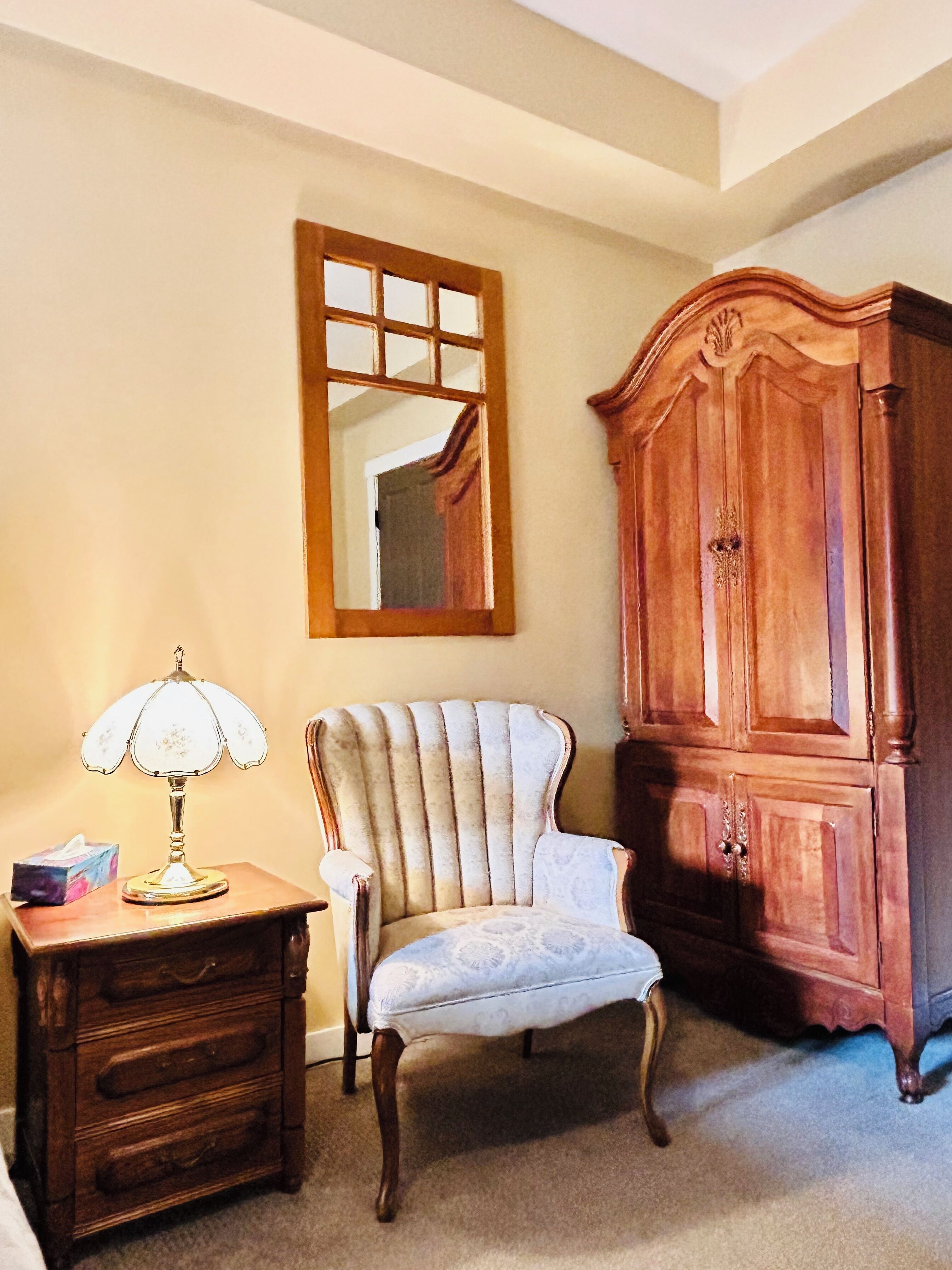 A room with a wooden cabinet, a chair, and a table with a lamp.