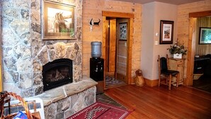 A stone fireplace with a framed picture above it, a water dispenser, a wooden door, and a dining area with a chair and table. - Bar 7 Ranch House - perfect for OHV travelers! (Meeker)