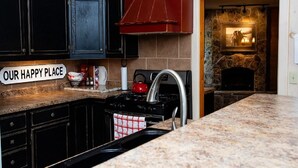 A kitchen with dark cabinets, a red hood, a stone fireplace, and a sign reading "OUR HAPPY PLACE". - Bar 7 Ranch House - perfect for OHV travelers! (Meeker)