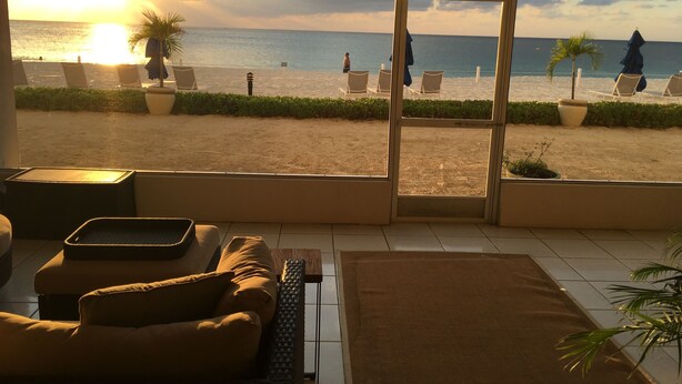 Une vue sur la plage depuis une chambre d’hôtel équipée d’un canapé, d’une table basse, et offrant une vue sur la plage avec des chaises et des parasols.
