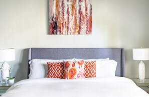 A hotel room with a bed, a grey headboard, and a wall with a colorful abstract painting. - Prime Residence #7 on 7 Mile Beach, High-End Ground Floor Beachfront Condo (George Town)
