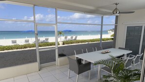 Un espace repas avec vue sur la plage, des chaises blanches, une table et un ventilateur de plafond.