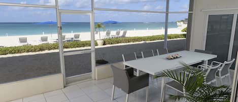 Un comedor con vista a la playa, sillas blancas, una mesa y un ventilador de techo.