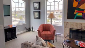 Un salon doté de deux grandes fenêtres, d’une cheminée, d’un fauteuil à rayures et d’un canapé.